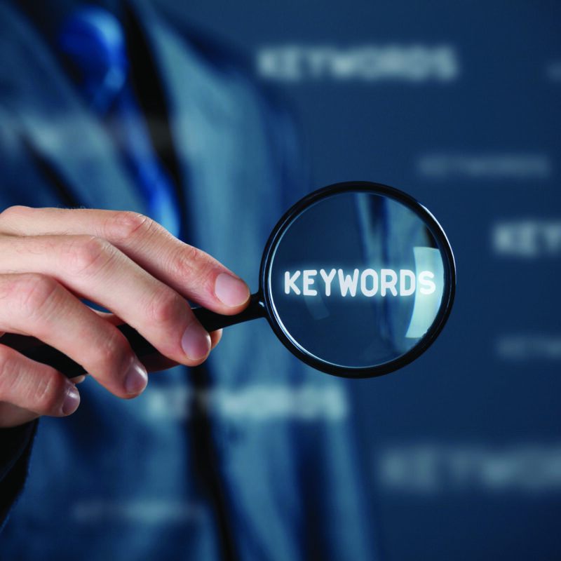 Looking for SEO Mistakes, a man holding a magnifying glass enlarges the term, 'keywords'.