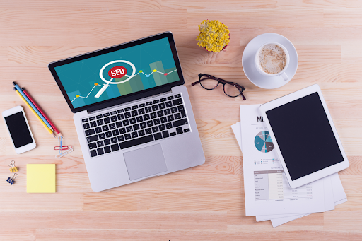 A laptop with "SEO" on the screen, papers, and a tablet on a desk.