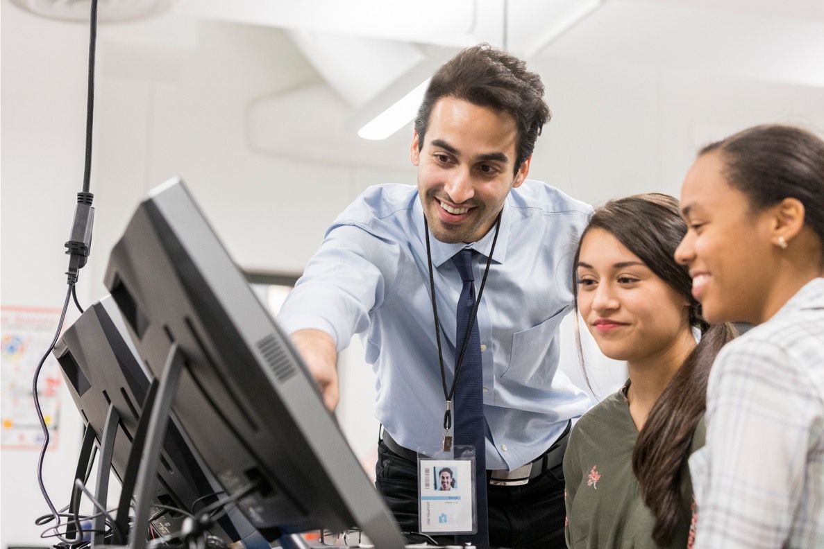 A teacher helping high-school students in web design class.