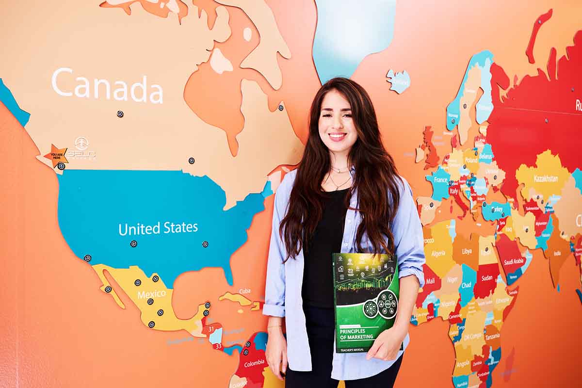 Student holding the Principles of Marketing textbook next to a global map on the wall